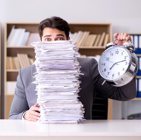 A man holding an alarm clock in front of a stack of papers.